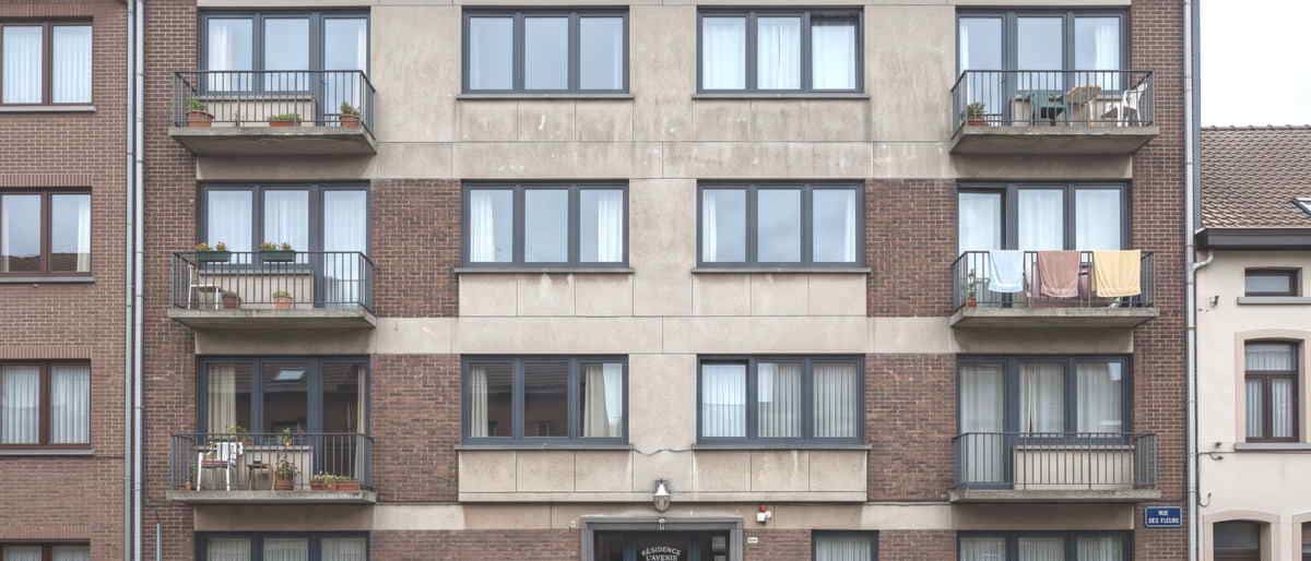 La façade d'un immeuble à appartements, fenêtres et balcons en enfilade, brique et béton enduit.