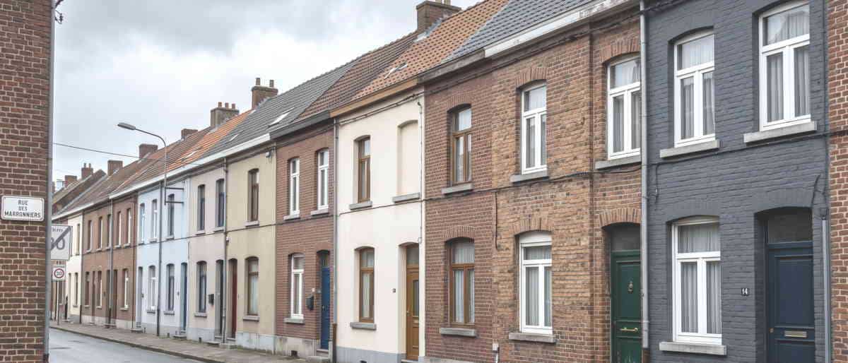 Une rangée de maisons mitoyennes en brique et en façade peinte, toits en tuiles, ciel gris.