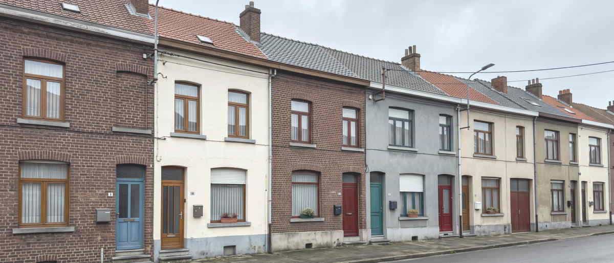 Une rangée de maisons mitoyennes aux façades de brique et de crépi, portes de couleur, jardinières aux fenêtres.